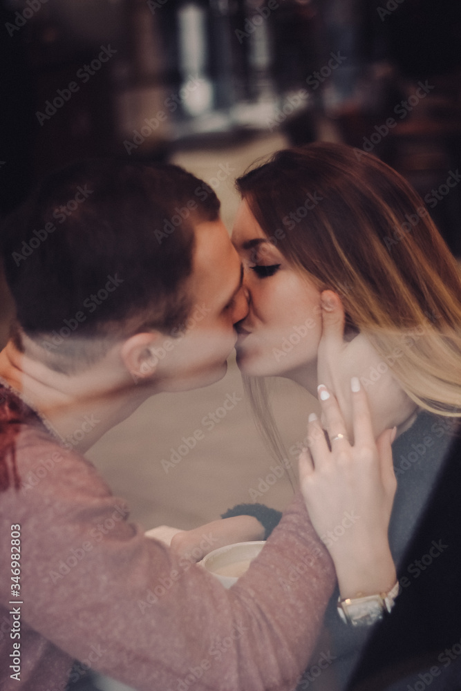 Fototapeta premium Cute brunette loving couple in cozy warm sweaters on a date at the cafe looking at the phone, using it. cold autumn, winter or spring day, european city. indoors