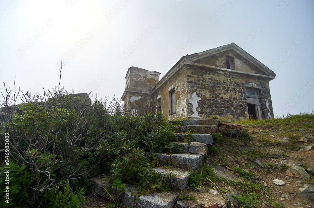 Old lighthouse in the fog on a cliff by the ocean. Gamow Lighthouse on the Gamow Peninsula. Dangerous Bay in the Sea of Japan. Far East. Old lighthouse in the fog on a cliff by the ocean. Gamow Lighthouse on the Gamow Peninsula. Dangerous Bay in the Sea of Japan. Far East.
