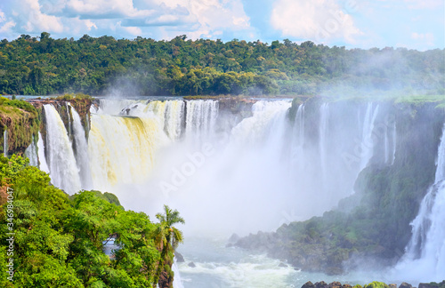 Iguazu waterfalls in Argentina  view from above. Panoramic view of many majestic powerful water cascades with mist. Panoramic image with reflection of blue sky with clouds.