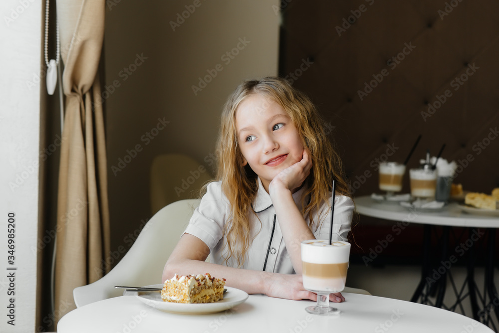 A cute little girl is sitting in a cafe and looking at a cake and cocoa close-up. Diet and proper nutrition A cute little girl is sitting in a cafe and looking at a cake and cocoa close-up. Diet and proper nutrition