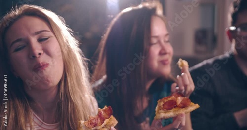 Multiracial happy young people eating pizza on sofa and laugh, cheerful students enjoying meal dining sitting together at home quarantine, diverse hungry friends sharing lunch at meeting