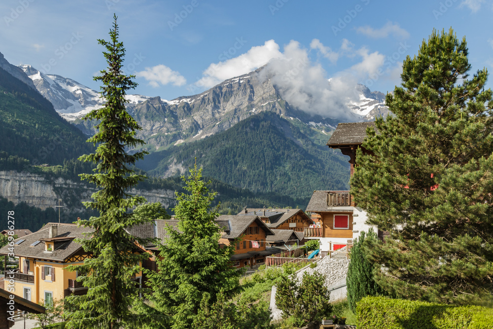 Amazing view of the snowy mountain peaks of the Swiss Alps from the small resort village of Champery in Switzerland. Bright blue sky and white fluffy clouds over rocky peaks. Chalets along the road