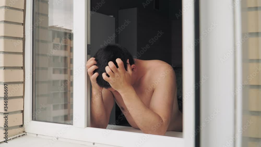Sad beautiful young guy is at home behind the window during the rain. Depression and loneliness Sad beautiful young guy is at home behind the window during the rain. Depression and loneliness