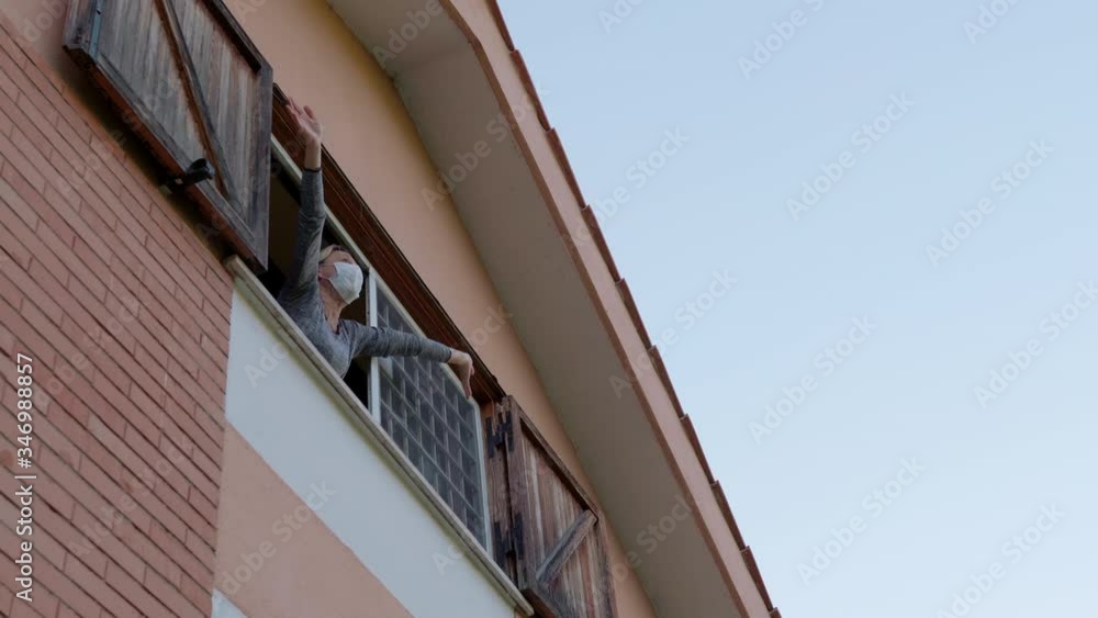 Coronavirus pandemic in Europe, viral infection outbreak. Grateful quarantined woman in mask applauding medical workers from the apartment window, health workers fighting against covid19 in hard Coronavirus pandemic in Europe, viral infection outbreak. Grateful quarantined woman in mask applauding medical workers from the apartment window, health workers fighting against covid19 in hard