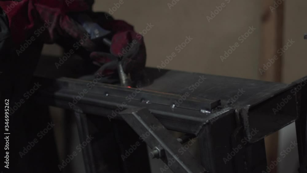 A welder welds metal parts using a welding machine. Detailed close-up. A welder welds metal parts using a welding machine. Detailed close-up.