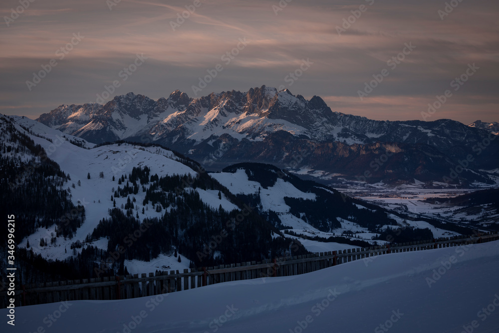 Mountains of mountain range Wilder Kaiser at Fieberbrunn during sunset in winter with snow, forest and valley, clouds in the sky, Tyrol Austria.