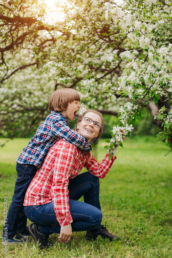 Fototapeta premium Mother and baby in blooming garden. Mom and child in spring. Springtime family scene. Flowers of apple or cherry tree.