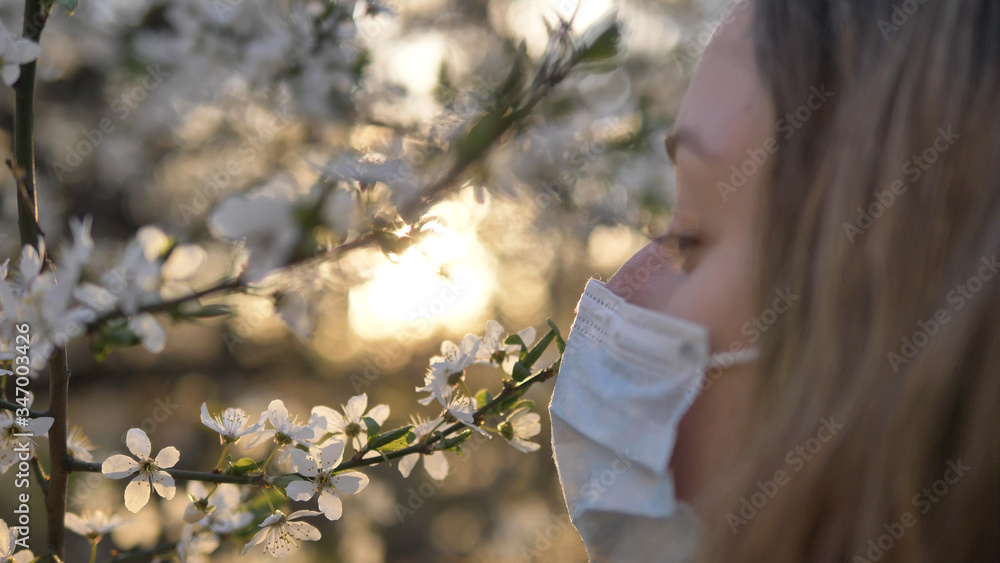 girl removes a medical mask and sniffs a blossoming tree of apple or cherry at sunset close-up, freedom aroma breathing walk in the fresh air