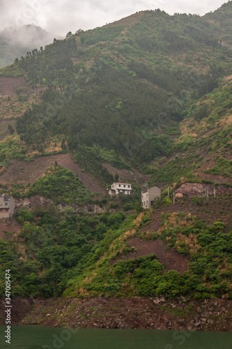 Shengli Street, China - May 6, 2010: Xiling gorge on Yangtze River. White and gray Farm houses on steep mountain slopes over which gray cloudscape descends. brown dirt and green foliage. photo