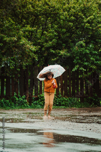 Happy child girl with umbrella and rubber boots jumping in a puddle. Cold spring rainy day © yanalev