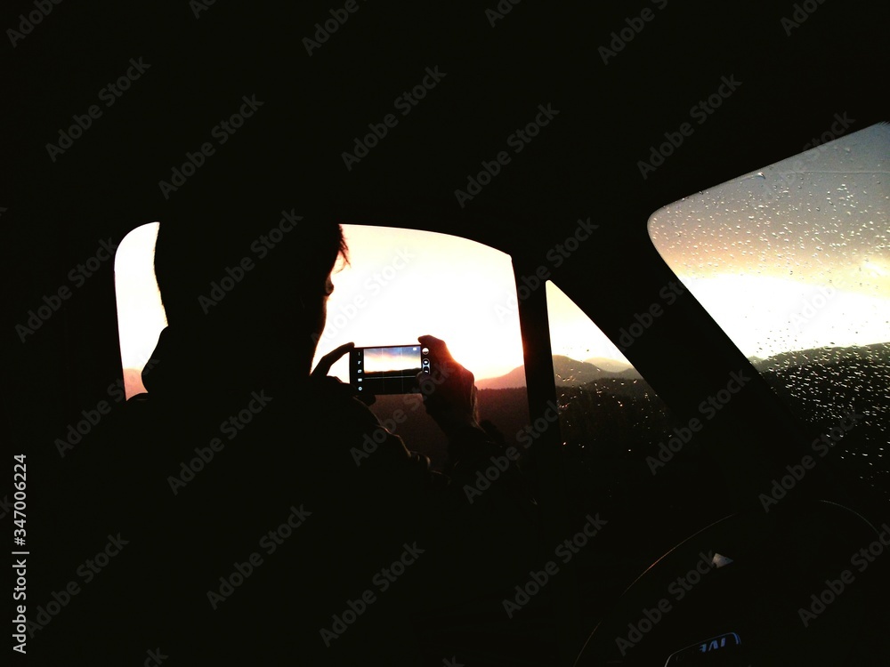 Silhouette Man Sitting In Car And Photographing With Smart Phone