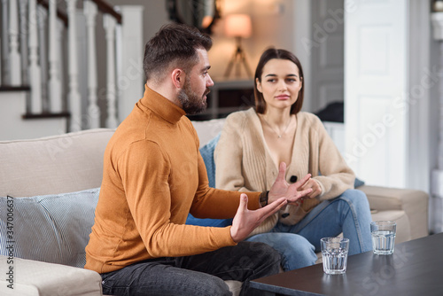Fototapeta Naklejka Na Ścianę i Meble -  Angry couple having argument or breakup. Young husband and wife having quarrel while sitting on a couch in the living room in a big house. Infidelity concept.