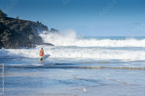 Surfer entering the water, while large waves crash. Hapuna Beach, Big Island Hawaii. 