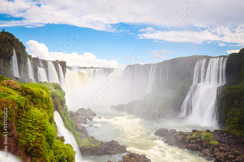 Iguazu waterfalls in Argentina, view from Devil's Mouth. Panoramic view of many majestic powerful water cascades with mist and low clouds. Panoramic image of Iguazu valley with blue sky and clouds.