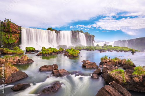 Majestic Iguazu waterfalls in Argentina. Panoramic view of many majestic powerful water cascades with mist and clouds. Panoramic image of Iguazu valley with grass and stones in calm water. photo