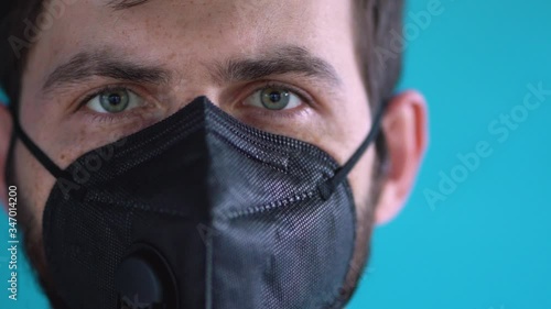 Wonderful bearded man with green eyes take off black face respirator mask against blue blurred background close up slow motion. Closeup guy portrait in lockdown period by corona virus threat. Safety. photo