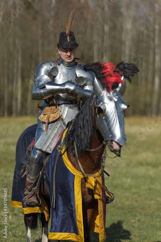 Young adult man in knightly armor rides across the field on a horse in armor Fototapeta