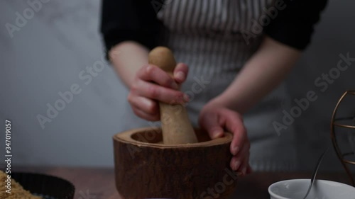 A woman hand crushing and grinding ingredients in a wooden mortar with a pestle into a fine powder.