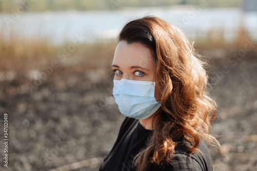 Portrait of woman wearing medical mask against the background of a river and scorched grass Coronavirus concept. Protect your health. 