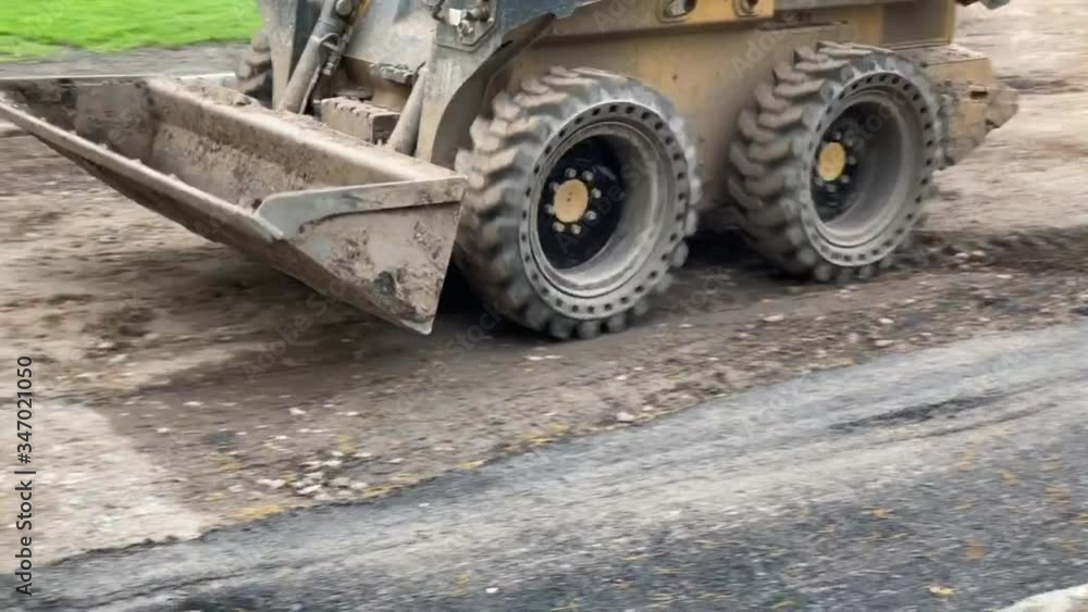 Construction equipment known as a skid steer clearing dirt from a road as it prepares for paving the street. Construction equipment known as a skid steer clearing dirt from a road as it prepares for paving the street.
