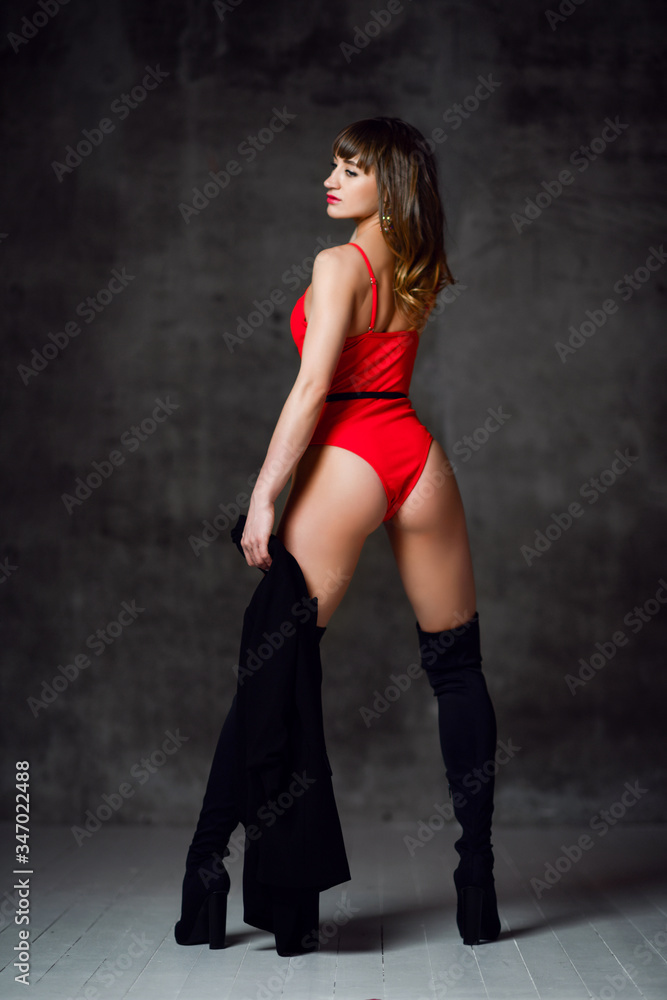 Young beautiful slim brunette woman in sexy red swimsuit or underwear and black high boots standing backwards Young beautiful slim brunette woman in sexy red swimsuit or underwear and black high boots standing backwards