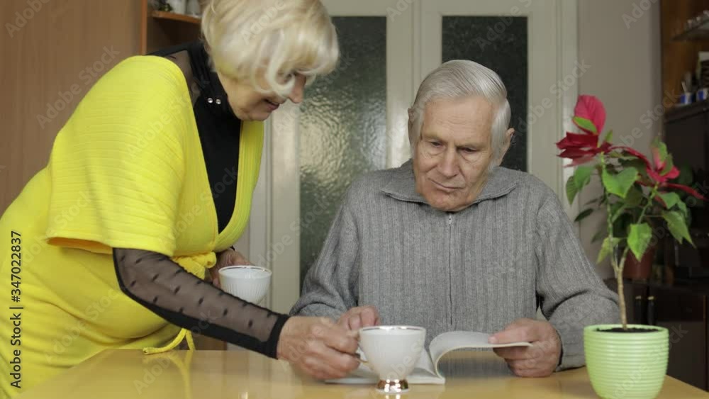 Happy old senior couple sit on table at home enjoying free time drink tea Happy old senior couple sit on table at home enjoying free time drink tea