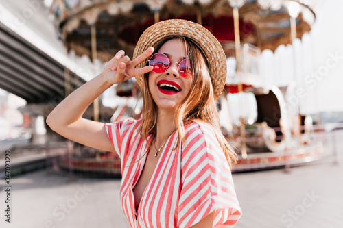 Stampa su Tela Outdoor portrait of stunning girl posing with peace sign near carousel