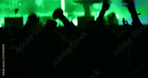 large crowd in green light silhouette of clapping hands at music festival stage