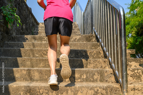 Cropped view of fitness runner woman training herself by running up steps on staircase in urban street. Uphill running can improve average running speed and your step length greater benefit. photo