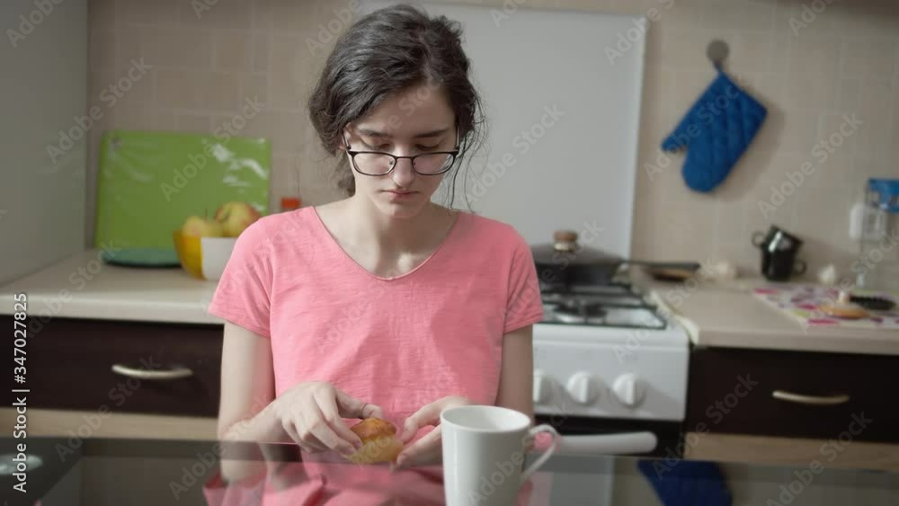 Attractive brunette girl eating a muffin, on the background of the kitchen Attractive brunette girl eating a muffin, on the background of the kitchen