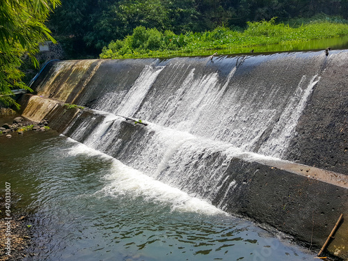 Photography of waterfall from the top of the Yellow River Dam in Sleman, Indonesia. The water runs through fish ponds and surrounding rice fields