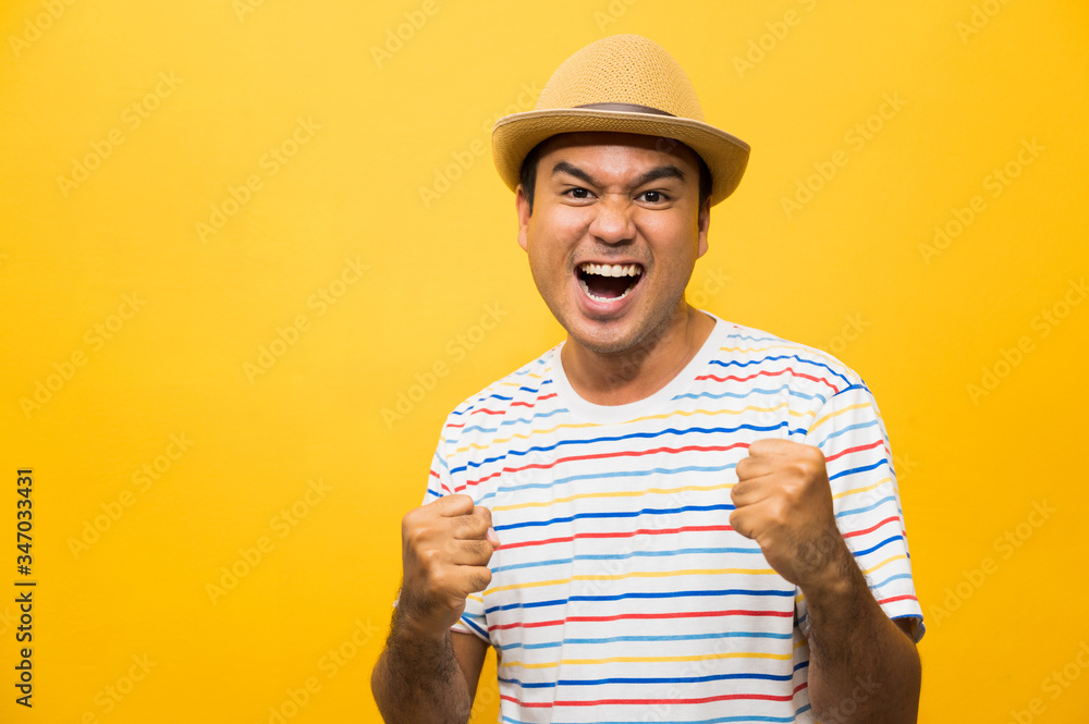 Happy young asian man celebrates with two hand in the air on yellow background. Happy young asian man celebrates with two hand in the air on yellow background.