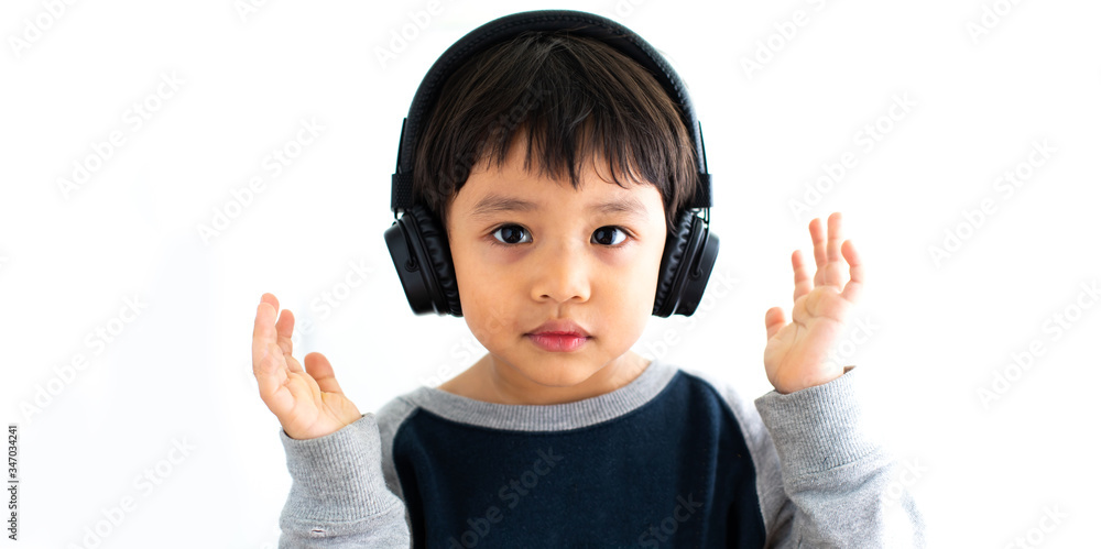 Family, home, technology and music concept. Portrait Young little Asian boy listening music with headphones at home. School child listening loud music in wireless earphones Family, home, technology and music concept. Portrait Young little Asian boy listening music with headphones at home. School child listening loud music in wireless earphones