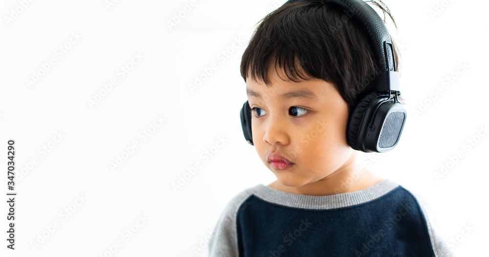 Family, home, technology and music concept. Portrait Young little Asian boy listening music with headphones at home. School child listening loud music in wireless earphones Family, home, technology and music concept. Portrait Young little Asian boy listening music with headphones at home. School child listening loud music in wireless earphones