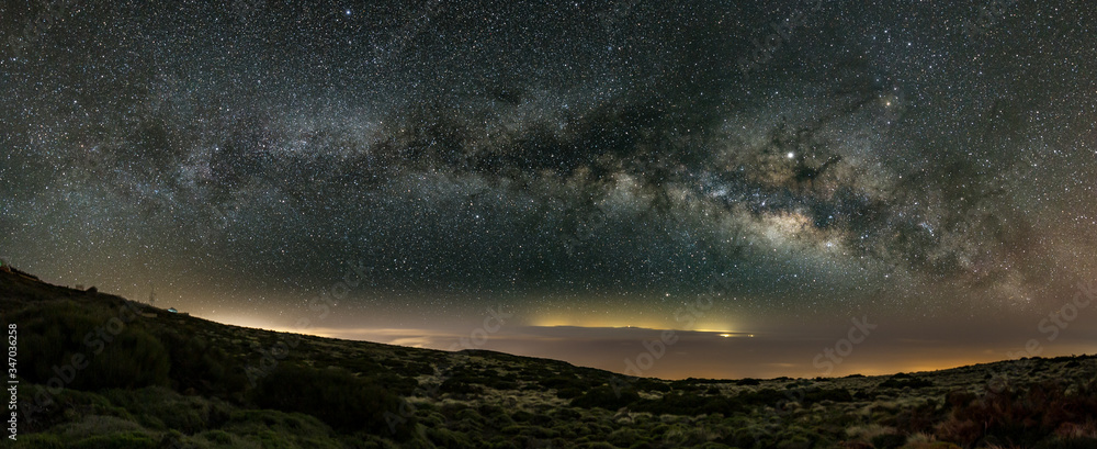 Milky Way in the spring sky above Teide National Park near Observatory. Jupiter is sparkling surrounded by star clusters and nebulae. Night lights over the coast and Gran Canaria in the background