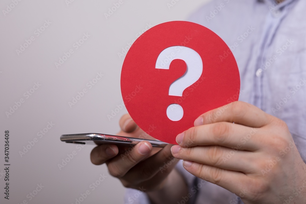 Φωτογραφία Sign of the question mark made of red paper and smartphone in the hands of a man