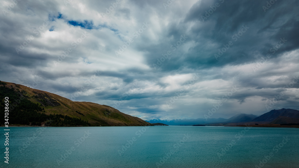 Dramatic view of Lake Pukaki with clouds gathering over the snow-capped mountain peaks. The alpine lake is famous for the amazing turquoise hues of the water and great mountain ranges in New Zealand. Dramatic view of Lake Pukaki with clouds gathering over the snow-capped mountain peaks. The alpine lake is famous for the amazing turquoise hues of the water and great mountain ranges in New Zealand.