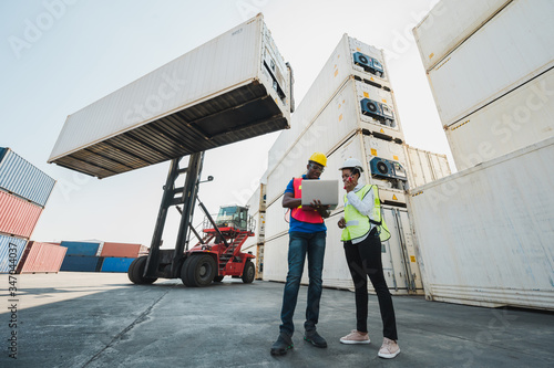 Two Black foreman man & woman worker working checking at Container cargo harbor holding laptop computer to loading containers. African dock male and female Logistics import export shipping concept.