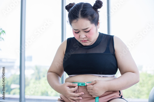 Asian overweight woman measuring fat layer with waistline at home