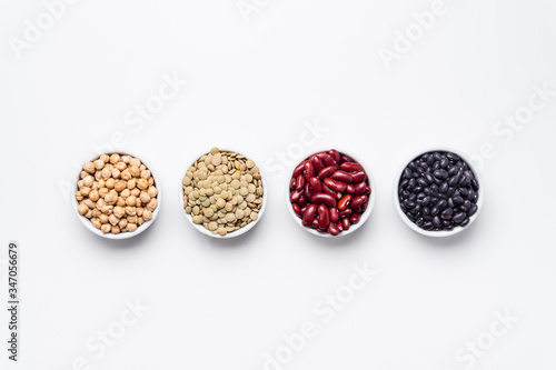 Bean bowls top view white background. These legumes are all pulses (dry edible plant seeds). The following ingredients can be seen: chickpeas, red kidney beans, green lentils and black turtle beans.