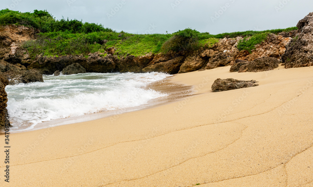 A clean beach with an ocean wave surrounded by rocks A clean beach with an ocean wave surrounded by rocks