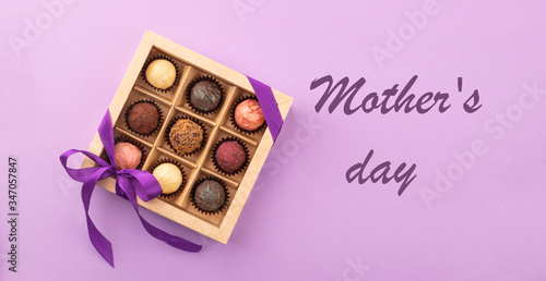 Set of different chocolates in a paper box with a satin ribbon on a bright background inscription Mother's Day.