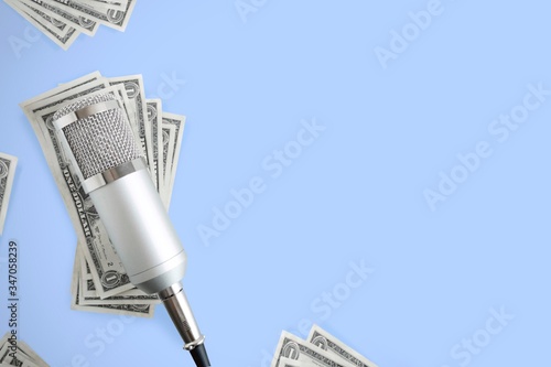 A silver microphone on money background, blue background and copy space. Concept of making money or earning money by Podcast.
