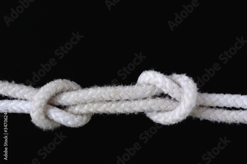 A white rope tied with fisherman knot on black background. © Siwapot Narukietmont