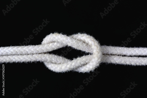 A white rope tied with square knot on black background. © Siwapot Narukietmont