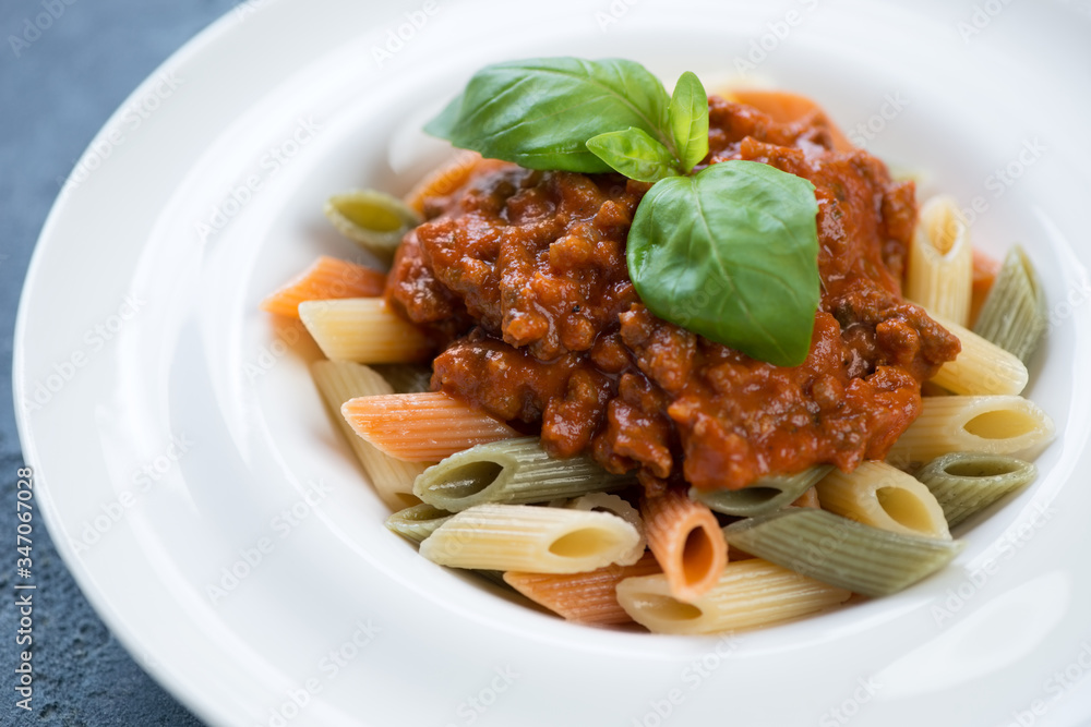 Close-up of penne pasta with bolognese sauce and fresh green basil in a white plate, selective focus Close-up of penne pasta with bolognese sauce and fresh green basil in a white plate, selective focus