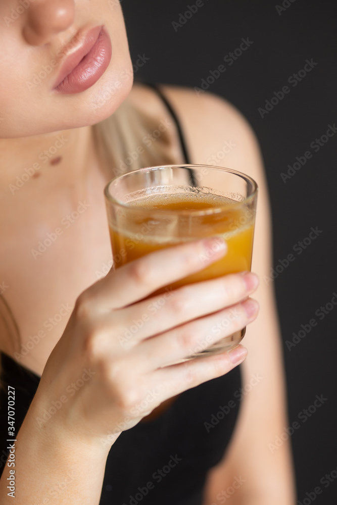 girl in sportswear drinks fresh orange juice on a dark background (close-up) girl in sportswear drinks fresh orange juice on a dark background (close-up)