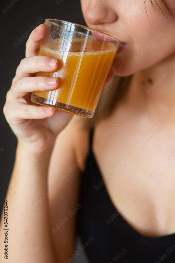 girl in sportswear drinks fresh orange juice on a dark background (close-up) girl in sportswear drinks fresh orange juice on a dark background (close-up)