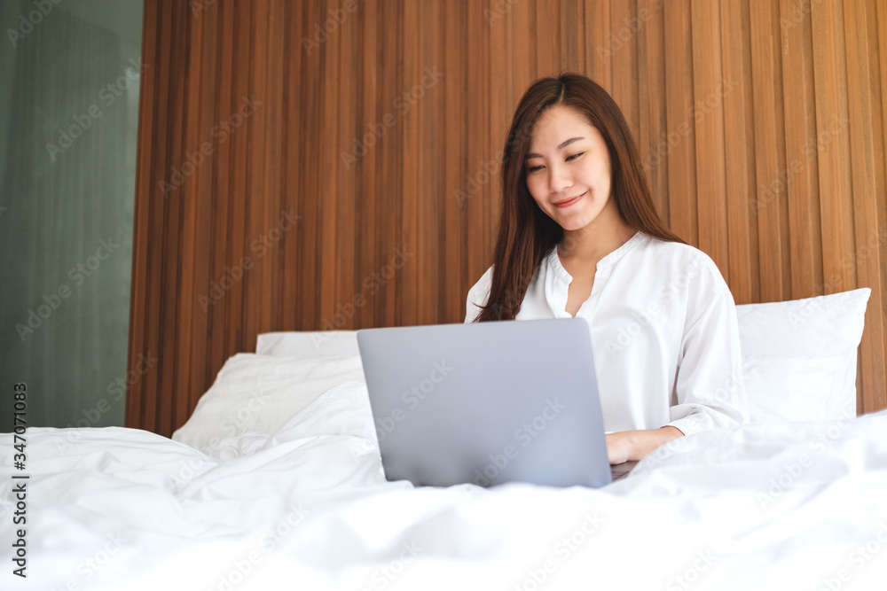 Closeup image of a beautiful woman using and working on laptop computer while sitting on a white cozy bed at home Closeup image of a beautiful woman using and working on laptop computer while sitting on a white cozy bed at home
