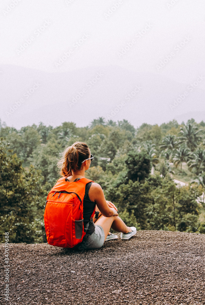 Woman tourist female with backpack is sitting on top of a mountain.